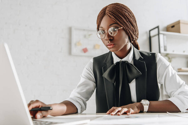 attractive focused african american adult businesswoman in glasses sitting at computer desk and working in office