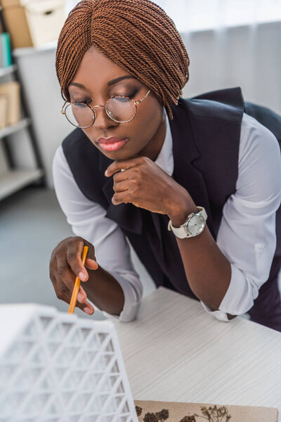 portrait of african american female adult architect in glasses holding pen and working on construction project in office