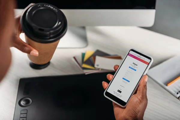 裁剪视图非洲裔美国女女商人拿着咖啡去和智能手机与 Instagram 应用程序在屏幕上 — 图库照片