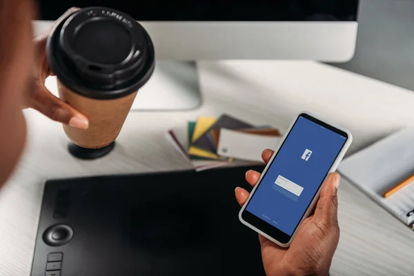 裁剪视图非洲裔美国女女商人拿着咖啡去和智能手机与脸书应用程序在屏幕上 — 图库照片