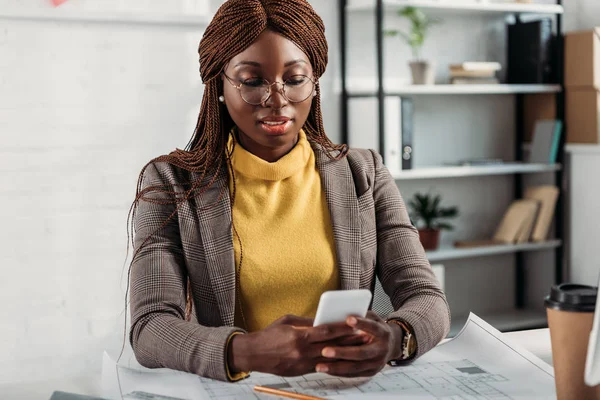 Hermosa Arquitecta Afroamericana Gafas Usando Smartphone Trabajando Escritorio Con Planos — Foto de stock gratis