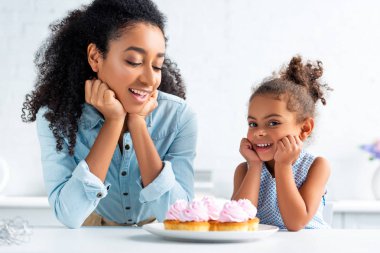mutlu Afrika kökenli Amerikalı anne ve kızı kekler mutfakta masada yakınındaki ellerinde çeneleri dinlenme