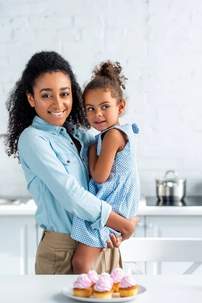 Happy African American Mother Hugging Daughter Kitchen Cupcakes Table — Stock Photo, Image