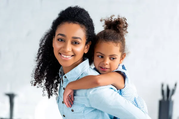 Smiling African American Mother Giving Piggyback Daughter Kitchen Looking Camera — Stock Photo, Image