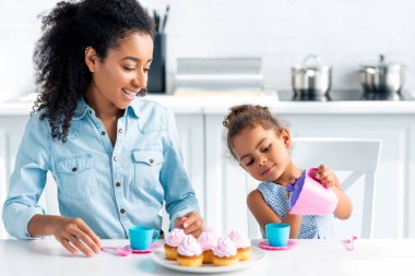 Afro-Amerikan kızı ve anne mutfakta plastik yemekleri ile oynamak