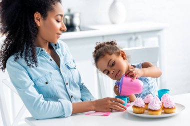 Afro-Amerikan kızı ve mutfak, çocuk çay dökme plastik yemekleri ile oynarken annesi