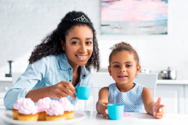 Afrika kökenli Amerikalı anne ve kızı ile plastik bardak tutan ve mutfak kamerada bakarak taçlar