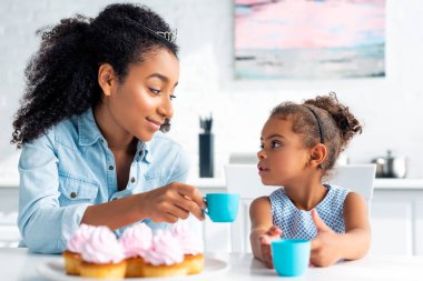 Afrika kökenli Amerikalı anne ve kızı ile plastik bardak tutan ve birbirine mutfakta bakarak taçlar