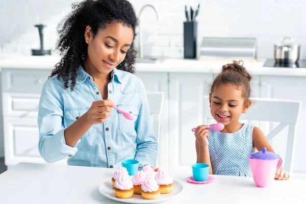 キッチンでカップケーキを食べるにアフリカ系アメリカ人の母と娘に行く  — 無料ストックフォト