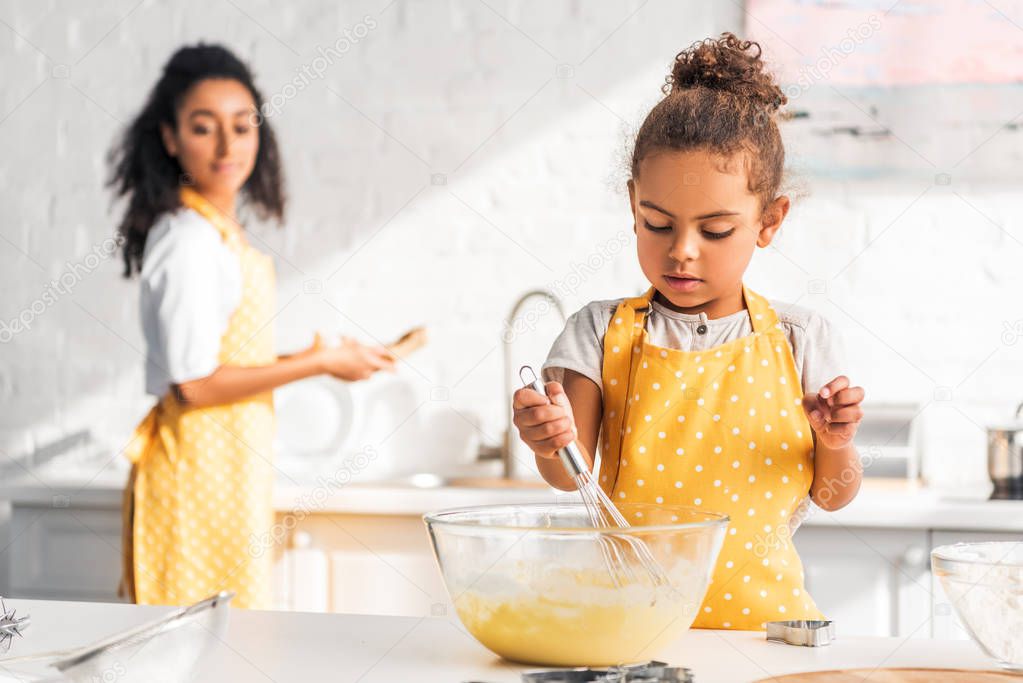 selective focus of african american daughter preparing and whisking dough in kitchen