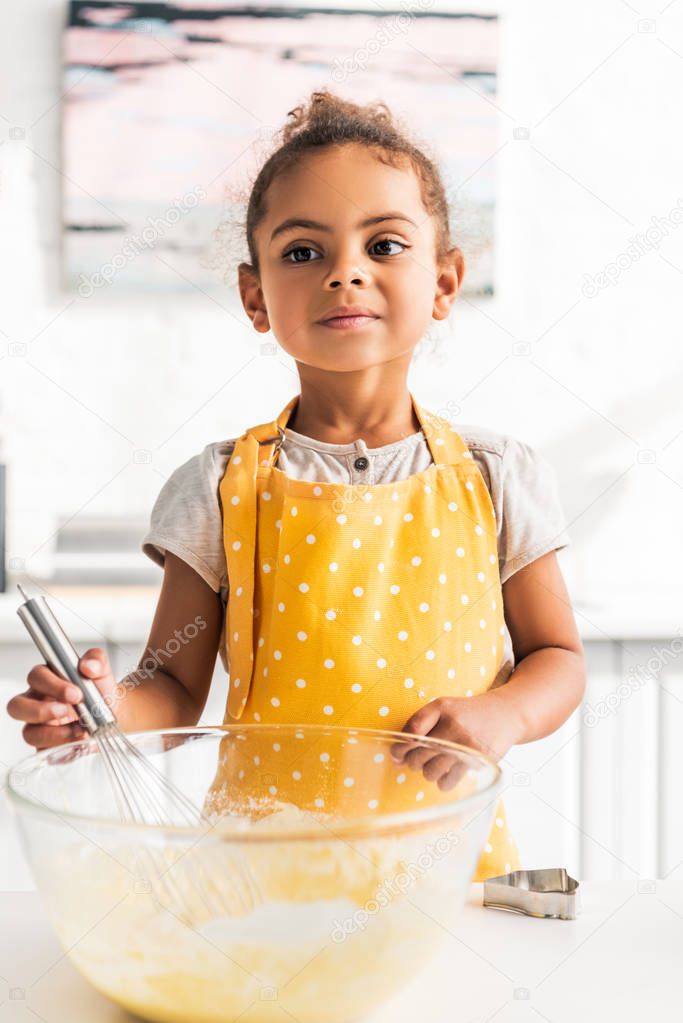 adorable african american kid preparing and whisking dough in kitchen