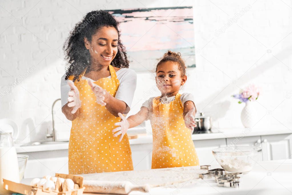 cheerful african american mother and daughter preparing dough and having fun with flour in kitchen