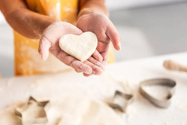 cropped image of african american kid holding heart shaped unbaked cookie in hands in kitchen