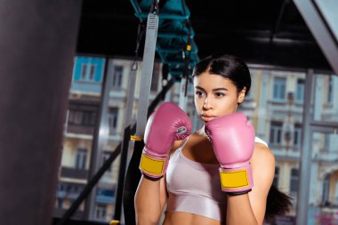 Attractive strong girl in protective gloves practicing boxing in gym  clipart