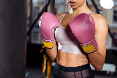 Partial view of strong girl in boxing gloves practicing boxing in gym  clipart