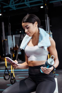 Spor salonunda spor şişe tutarken dijital aygıt kullanan güzel sportif kız 