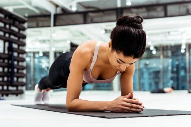 Beautiful sportive girl doing plank on mat  in fitness gym clipart