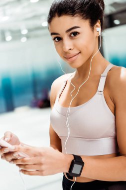 Fitness salonunda müzik dinlerken kameraya gülümseyen çekici sportif kız