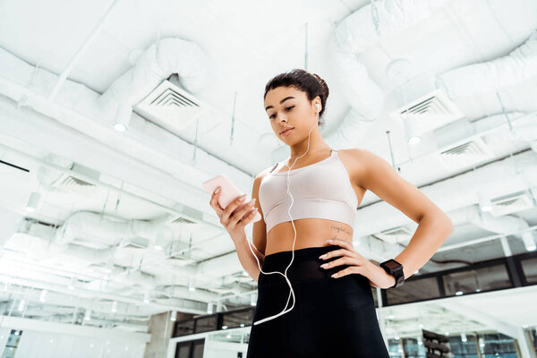 Low angle view of beautiful sportive girl listening to music while standing in fitness gym