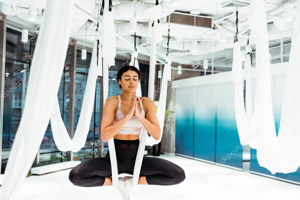 Girl practicing antigravity yoga in lotus position with namaste mudra gesture in light studio