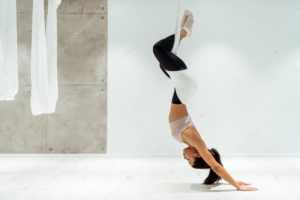 Sportive girl relaxing while practicing antigravity yoga and inversion position in yoga studio