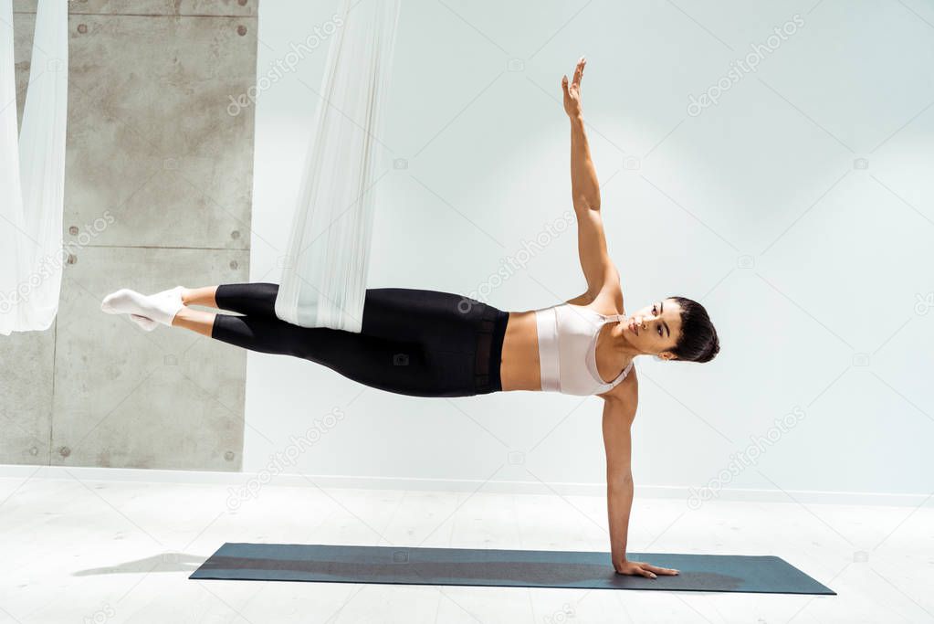 Attractive strong female practicing antigravity yoga in hammock in studio