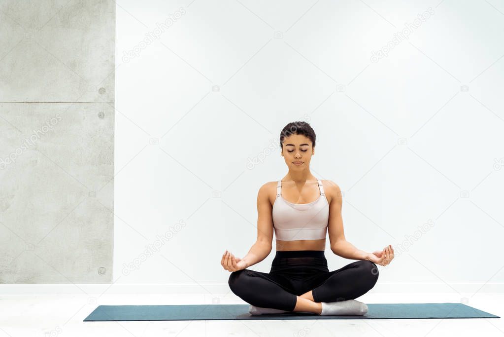 Relaxed girl with closed eyes meditating in lotus position in yoga studio