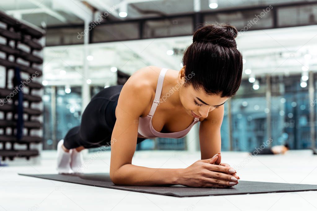 Beautiful sportive girl doing plank on mat  in fitness gym