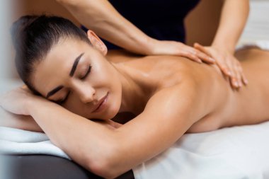 beautiful young woman with closed eyes having massage in spa  clipart
