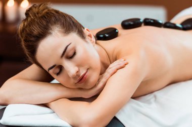 güzel genç kadın kapalı gözlerle spa salonda sıcak taş masaj keyfi 