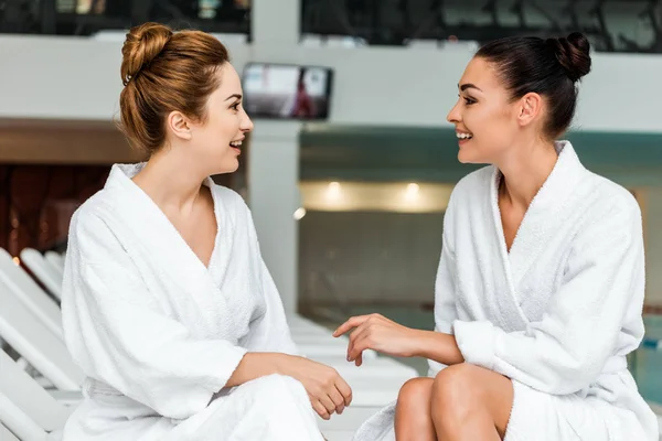 美丽的微笑的年轻妇女在浴袍说话和看着对方 而在水疗休息 — 免费的图库照片