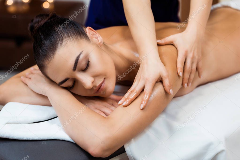 attractive young woman with closed eyes having massage in spa 