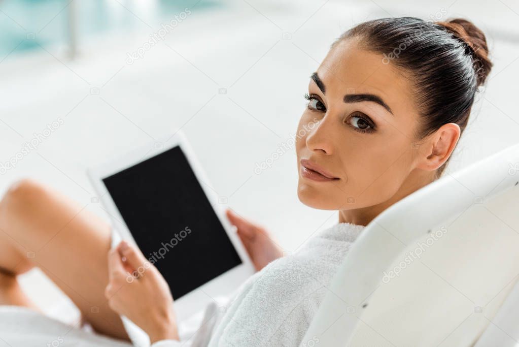 beautiful woman holding digital tablet with blank screen and looking at camera in spa 