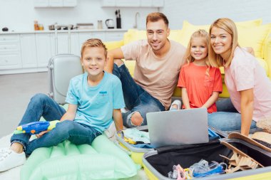 mutlu aile dizüstü bilgisayar kullanarak, yaz tatil planlama, Bagaj paketleme ve harika vakit geçiriyor seyahat kavramı