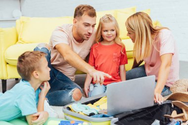 mutlu aile dizüstü bilgisayar kullanarak, yaz tatil planlama, Bagaj paketleme ve harika vakit geçiriyor seyahat kavramı