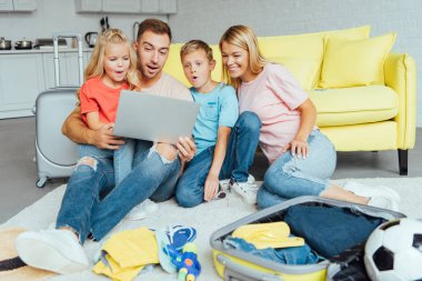 mutlu aile dizüstü bilgisayar kullanarak, yaz tatil planlama, Bagaj paketleme ve harika vakit geçiriyor seyahat kavramı