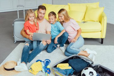 mutlu aile dizüstü bilgisayar kullanarak, yaz tatil planlama, Bagaj paketleme ve harika vakit geçiriyor seyahat kavramı