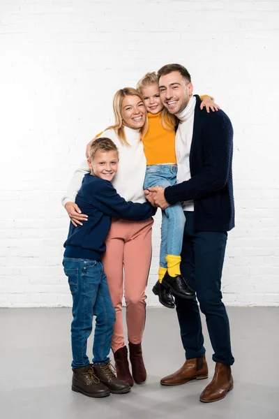 smiling family in casual clothes hugging and looking at camera on white background