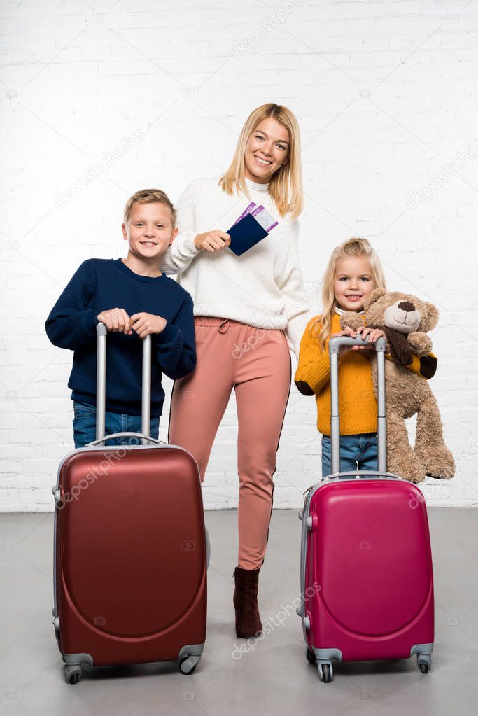 Happy mother holding passport and tickets while children holding suitcases ready to go on winter trip