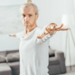 Selective focus of man standing in warrior yoga pose at home