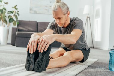 atletik yetişkin adam oturan ve evde yoga mat germe spor giyim