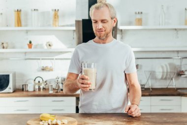 Yetişkin sportif adam holding cam muz protein içeceği evde ile gülümseyen