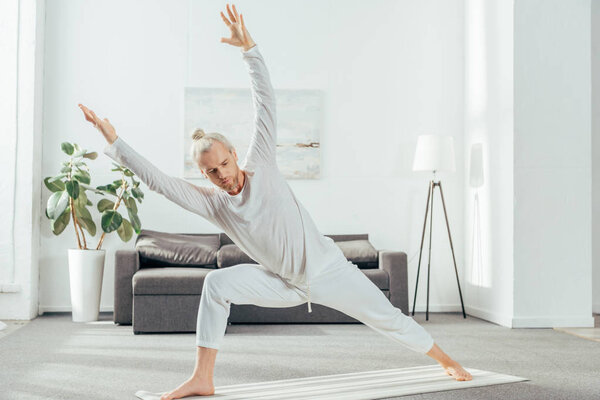 athletic adult man practicing yoga on mat at home