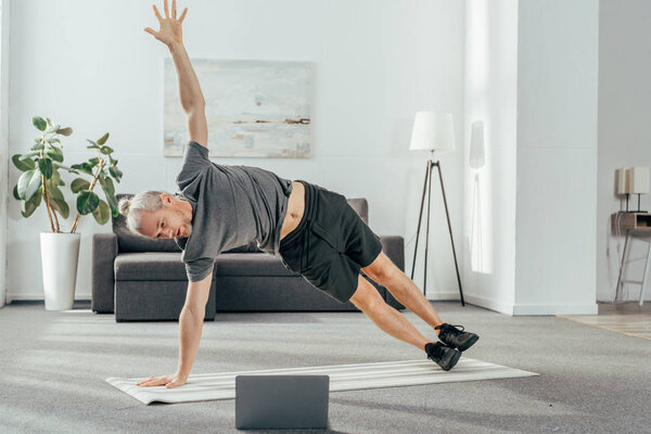 athletic man in sportswear practicing side plank and looking at laptop