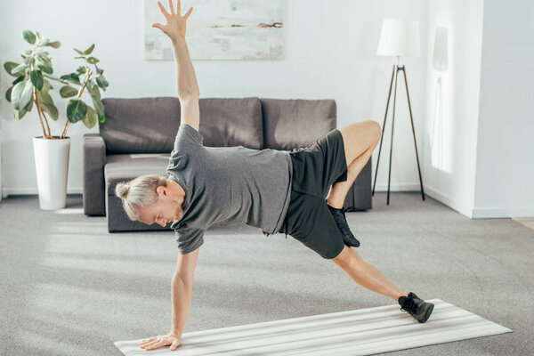 high angle view view of athletic man in sportswear practicing side plank on yoga mat at home 