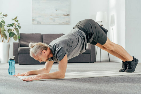 side view of athletic adult man in sportswear exercising on yoga mat at home