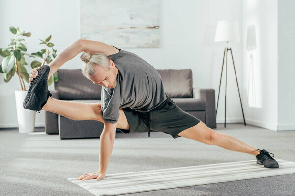 sporty adult man balancing and stretching on yoga mat at home 