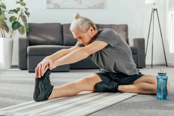 运动成人在运动服坐和伸展瑜伽垫在家里 — 图库照片