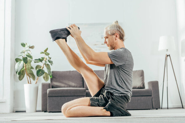 side view of sporty adult man stretching on yoga mat at home