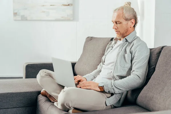 Schöner Erwachsener Mann Sitzt Auf Der Couch Und Benutzt Laptop — kostenloses Stockfoto